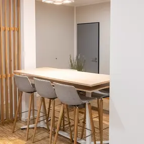 Moderner Wartebereich mit Holztisch, vier grauen Stühlen und heller, freundlicher Büroeinrichtung.