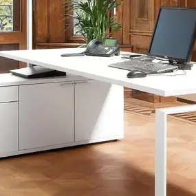 Moderner, weißer Schreibtisch mit Computer und Telefon in stilvollem Büro mit Holzvertäfelung.