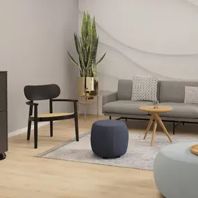 Modern eingerichteter Wartebereich mit grauem Sofa, Pflanzen, Couchtisch, Sitzhockern und Sideboard.