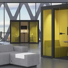 Moderne Büroeinrichtung mit gelben Akustikboxen, Schreibtischen und grauen Sofas in offenem Workspace.