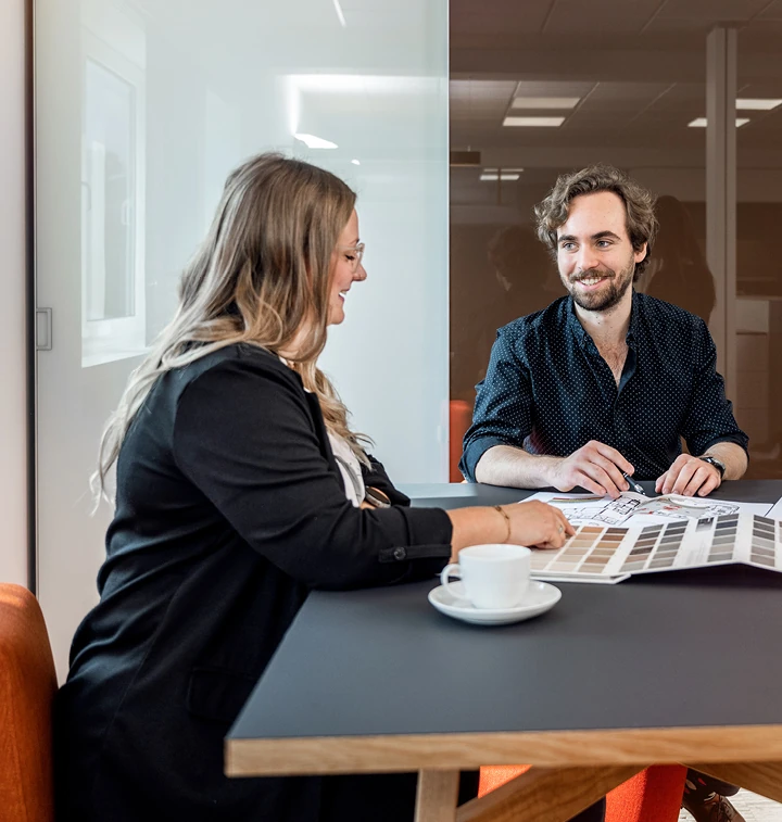Zwei Personen besprechen Farb- und Materialmuster bei einer Innenarchitektur-Beratung am Tisch.